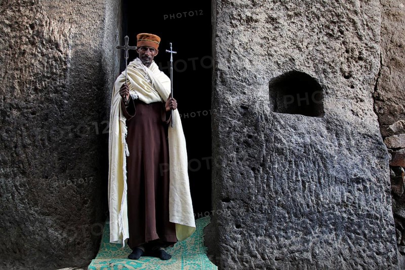 Priest with crosses standing in stone niche, Lalibela, Lasta Mountains, Ethiopia