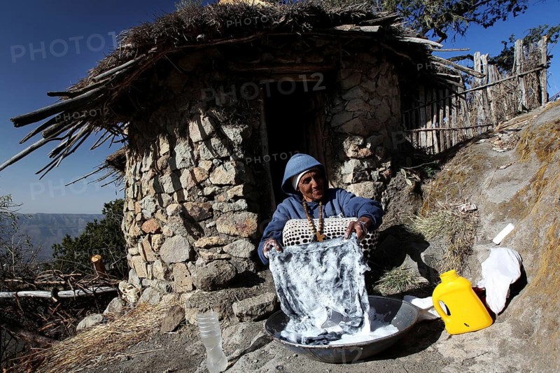 Woman washing in front of a traditional round hut with picturesque views of Lasta Mountains, Lalibela, Amhara, Ethiopia