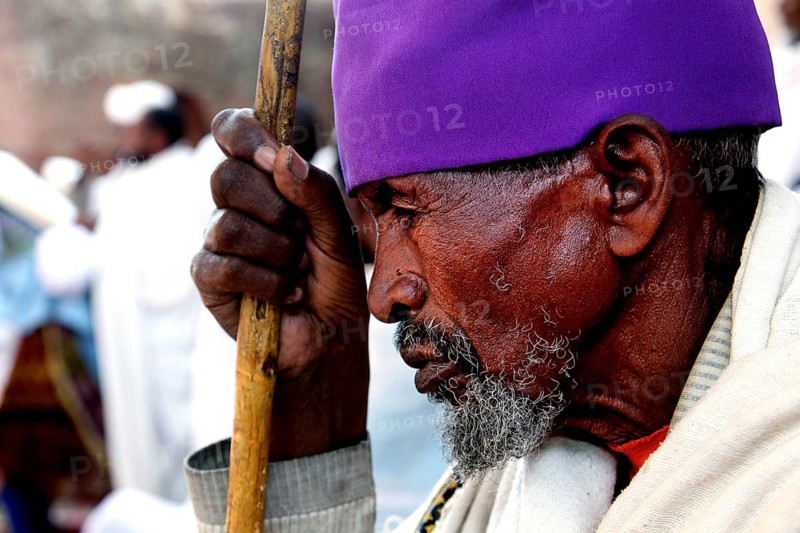 An elderly man wearing purple head covering prays at Bete Maryam church during Easter, Lalibela, Amhara, Ethiopia