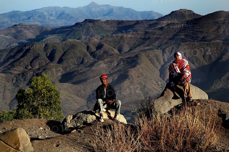 Two people sit in front of the impressive mountain scenery of the Lasta Mountains, Lalibela, Amhara, Ethiopia