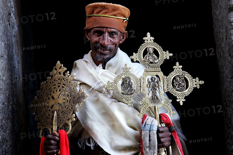 Priest with decorative crosses in traditional robes against dark background, Lalibela, Lasta Mountains, Ethiopia