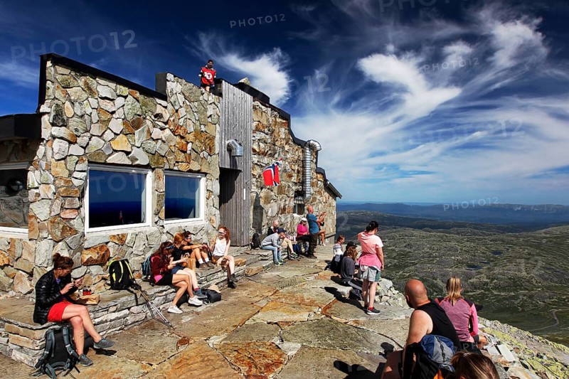 Stone hut on a summit plateau with visitors enjoying the view, Hardangervidda, Gausdal, Norway