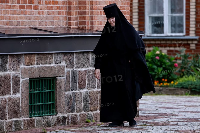 Nun in black clothes walks along the stone wall of the church, Kuremäe, Pühtitsa, Estonia