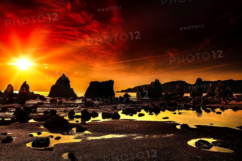 Fiery red sunrise over coastal rock formations with intense reflections, Kushimoto, Japan