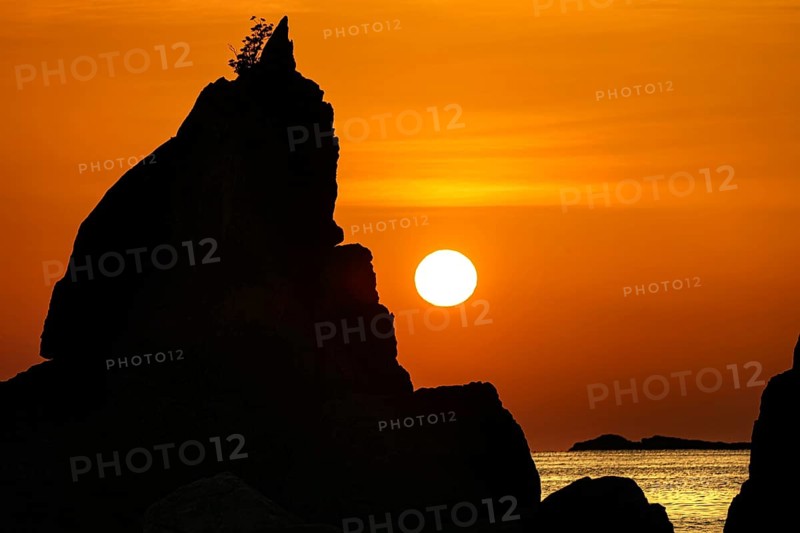 Single tall rock formation in glowing sunrise on the coast, Kushimoto, Japan