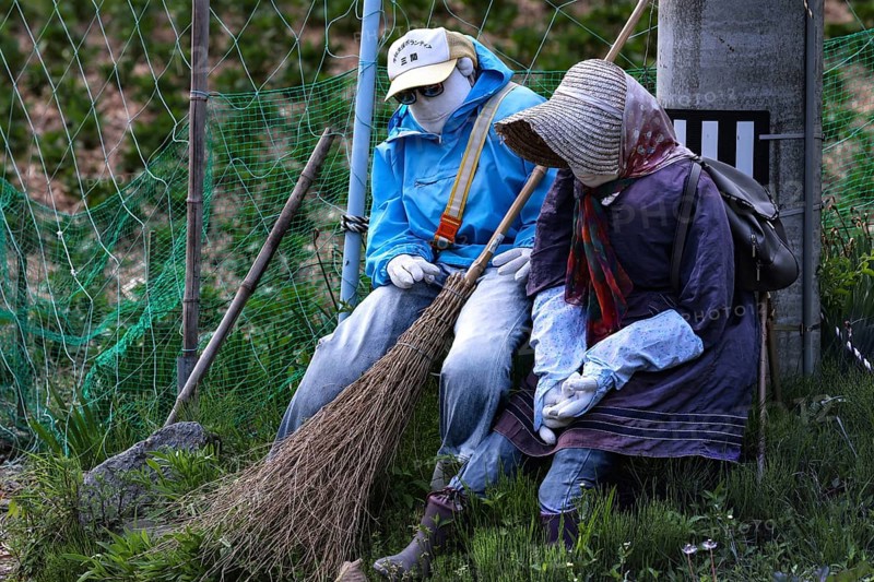 Two fabric figures sitting in the garden holding brooms