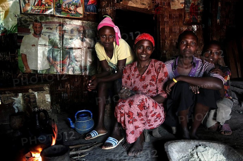 Woman with her daughters in a hut sitting together at a fireplace, Yirga Alem, Ethiopia