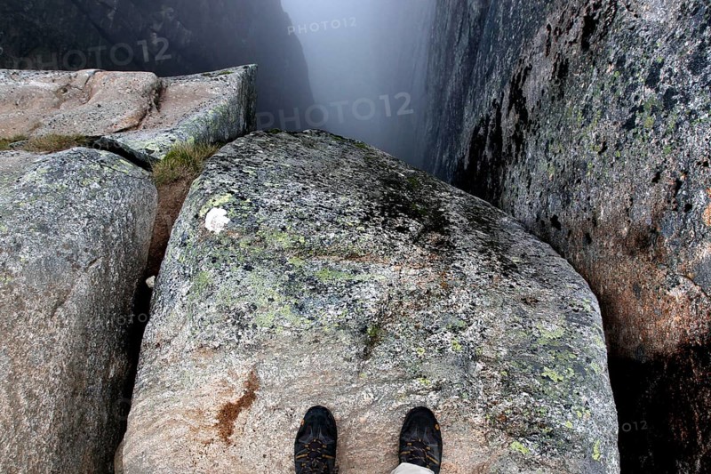 Two feet stand on a rock looking into the depths of Kjeragbolten, Lysefjord, Rogaland, Norway