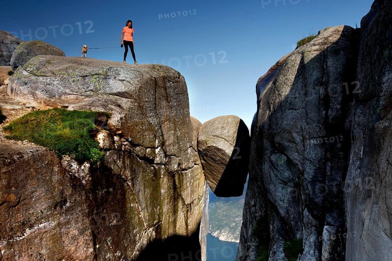 Tourist standing with her dog on a rock near Kjeragbolten with a view of the valley, Lysefjord, Norway