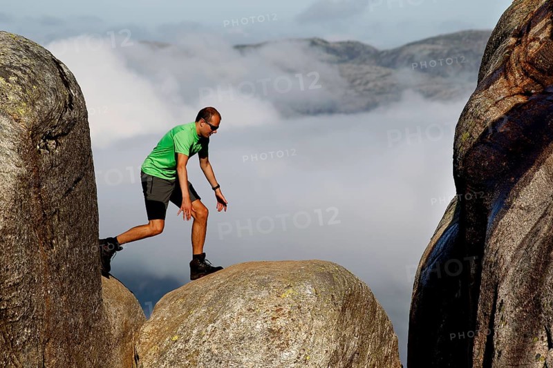 Tourist balancing on Kjeragbolten between rocks high above the clouds, Lysefjord, Norway