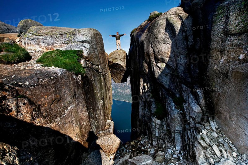 Daring person standing on the impressive Kjeragbolten above the fjord, Lysefjord, Norway