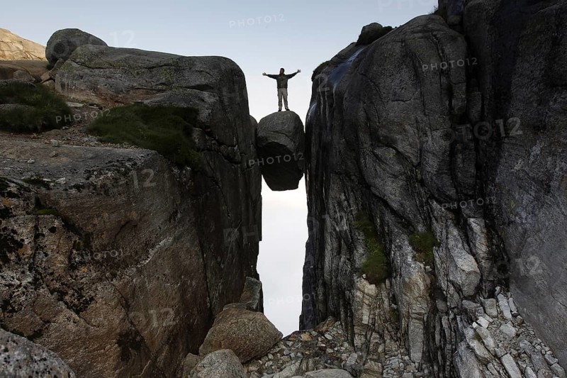 Adventurous person balancing on floating Kjeragbolten, Lysefjord, Rogaland, Norway