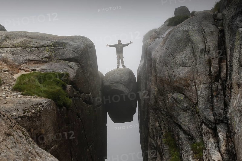 Person standing on Kjeragbolten rock hanging in the air, Lysefjord, Rogaland, Norway