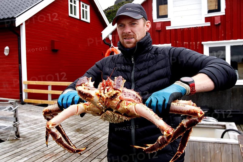 Man holding huge king crab standing outside near red buildings, Sarnes, Norway