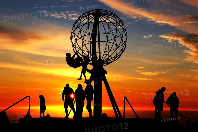 Silhouettes of people on the North Cape globe in front of a glowing sunset, North Cape, Magerøya, Norway