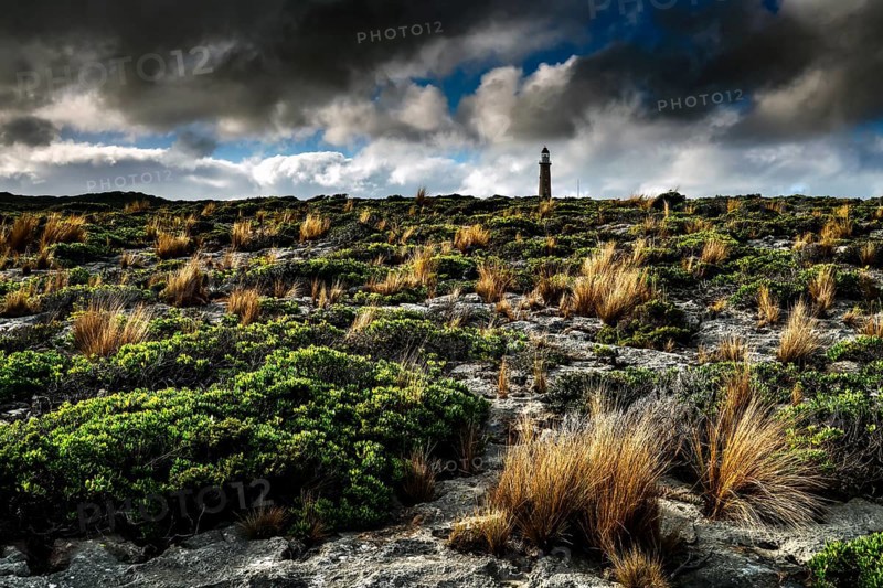 A lighthouse stands out in rugged vegetation under a dramatic sky near Cape du Couedic, Kangaroo Island, South Australia, Australia
