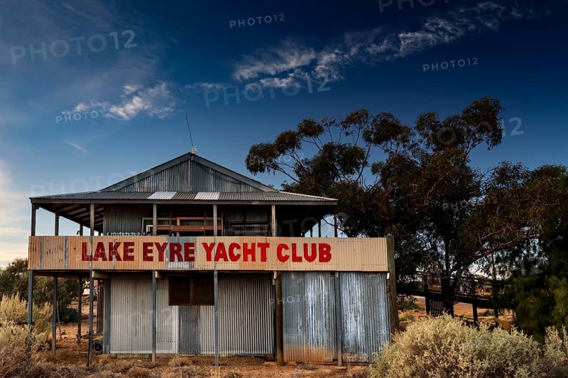 Dilapidated Lake Eyre Yacht Club building with eye-catching sign and trees, Marree, South Australia, Australia