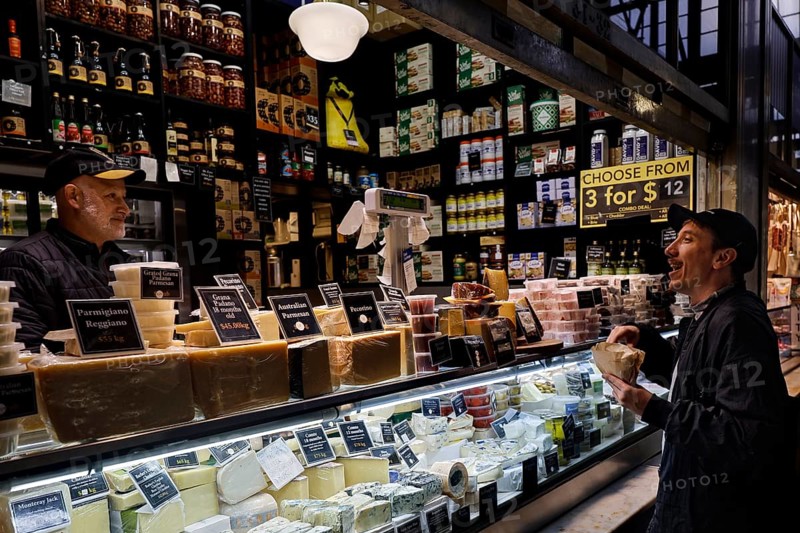 Sales stand with diverse delicacies and interacting customers at Queen Victoria Market, Melbourne, Victoria, Australia