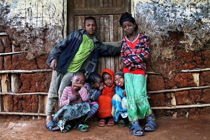 Children in colorful clothes pose happily in front of a traditional house, Dorze village, Ethiopia