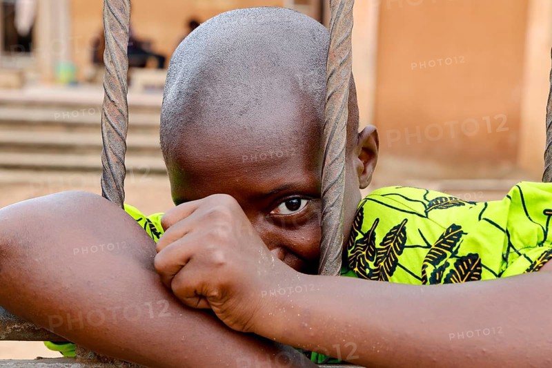 A child looks through metal mesh, a soft smile on his face, Bouké, region, Côte d'Ivoire