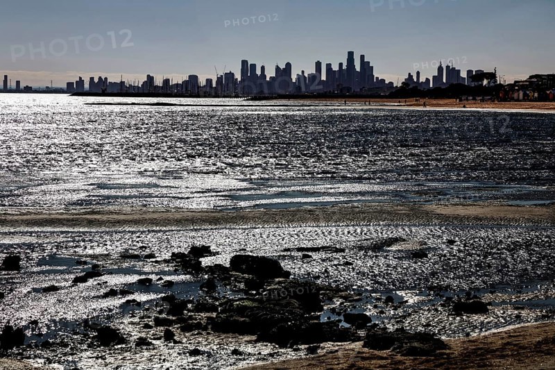 Melbourne skyline seen from Brighton Beach with reflecting sun rays on the water's edge, Brighton Beach, Melbourne, Victoria, Australia