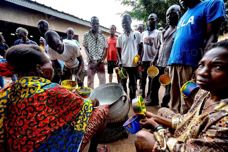 Men standing and sitting serving food at Saint Camille men's psychiatry, Bouaké, Côte d'Ivoire