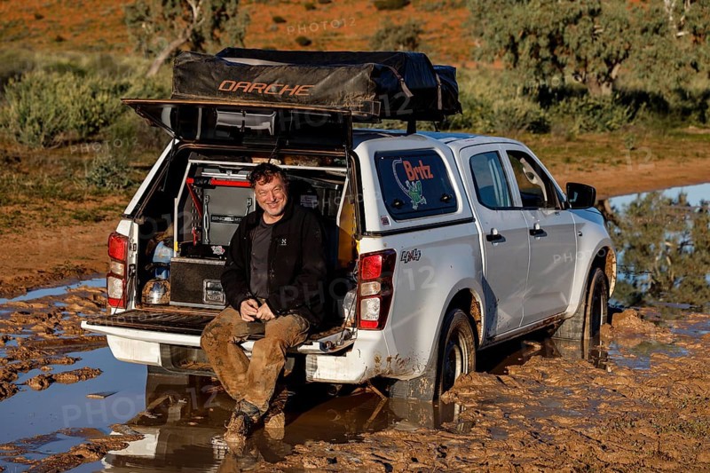 Man sits relaxed in the open trunk of a muddy off-road car on the Old Andado Track