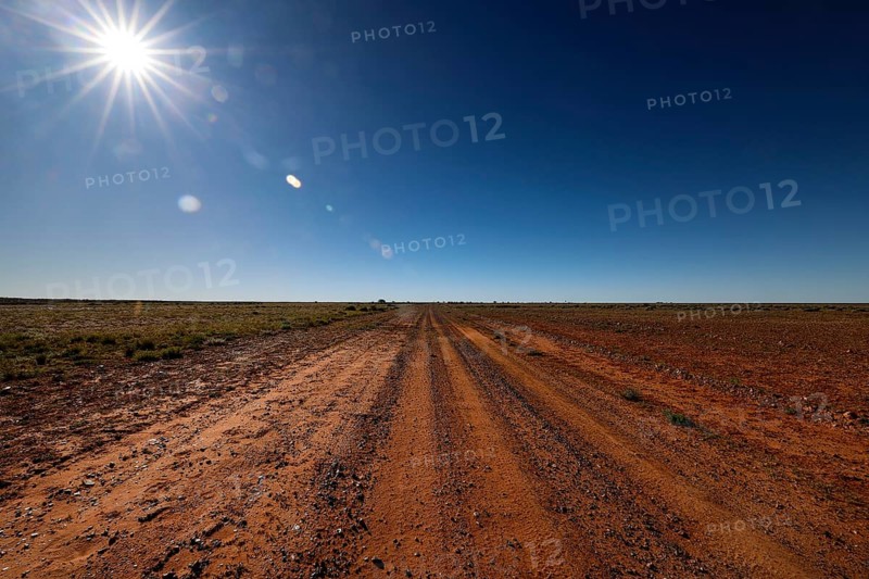Dusty desert trail under bright sun and clear sky, Old Andado Track, Northern Territory, Australia
