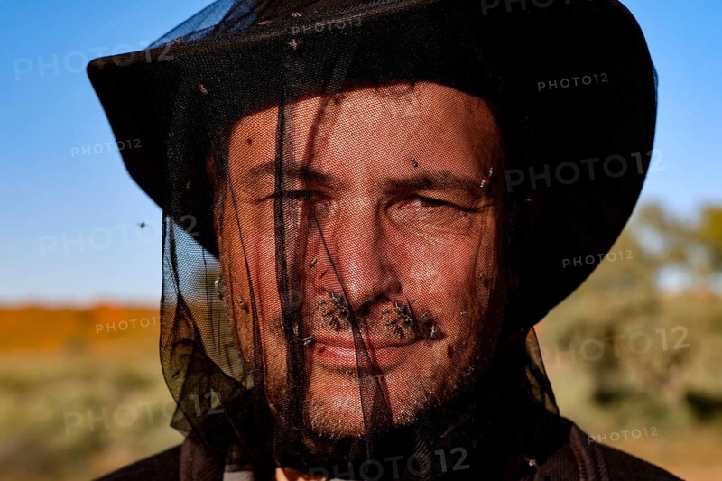 Man with a fly net over his face in front of a clear sky