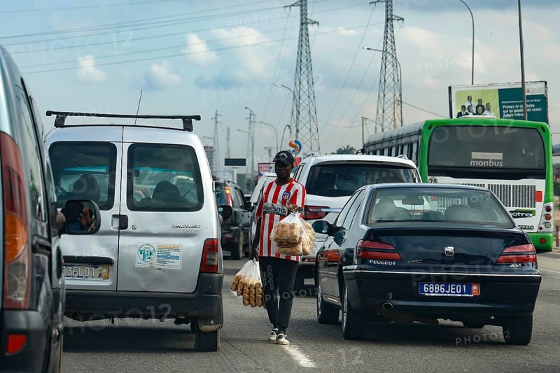Hustle and bustle in Abidjan with cars stuck in traffic and a person crossing the road, Abidjan, null, Côte d'Ivoire