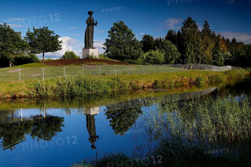 Socialist statue in Grutas Park is reflected in a calm body of water surrounded by trees, Druskininkai, Lithuania