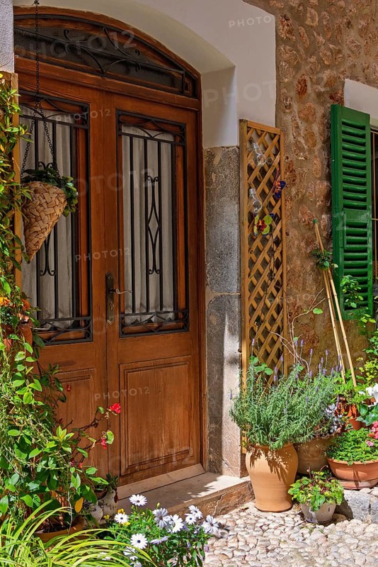 Garden flowers in pots by a wooden door to a idyllic residential house in a village, Fornalutx, Mallorca, Spain