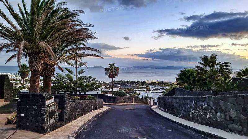 View of a road with palm trees leading to the sea, in the background the island of Fuerteventura at dusk, Playa Blanca, Lanzarote