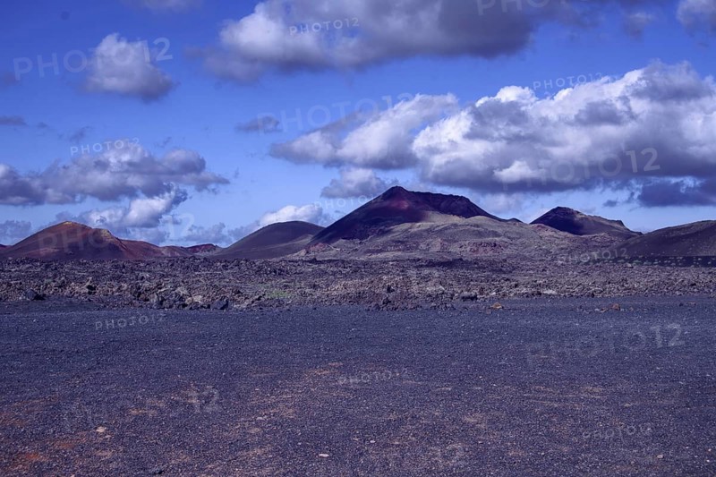 View of a vast volcanic landscape with colorful mountains under a cloudy sky, Tinajo Lanzarote