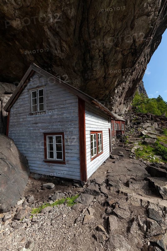 Historical wooden houses sheltered under a massive rock overhang. Summer, Helleren (Helleren), Rogaland, Norway