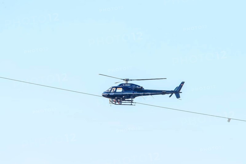 A blue helicopter flies in a clear sky. Technical details are visible, marking work on a new high-voltage line, Lemförde, Lower Saxony, Germany