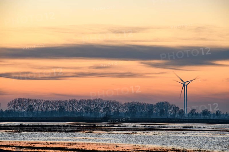 A wind turbine at sunset next to a calm body of water and trees, wind turbines in front of an orange sunset with trees as silhouettes, Hüde, Dümmer nature park Park, Lower Saxony, Germany