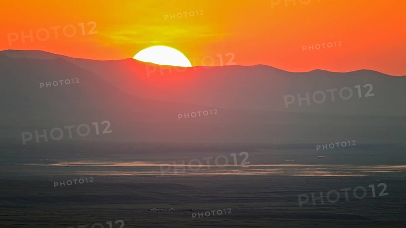 Sunrise with red fireball of rising sun over mountain ridges and extensive steppe landscape in the lowlands of a river with yurts and horses, Bulgan, Mongolia