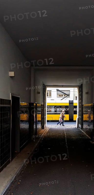 View through a corridor to the backyard onto Chässeestraße with passengers and moving tram, Berlin, Germany