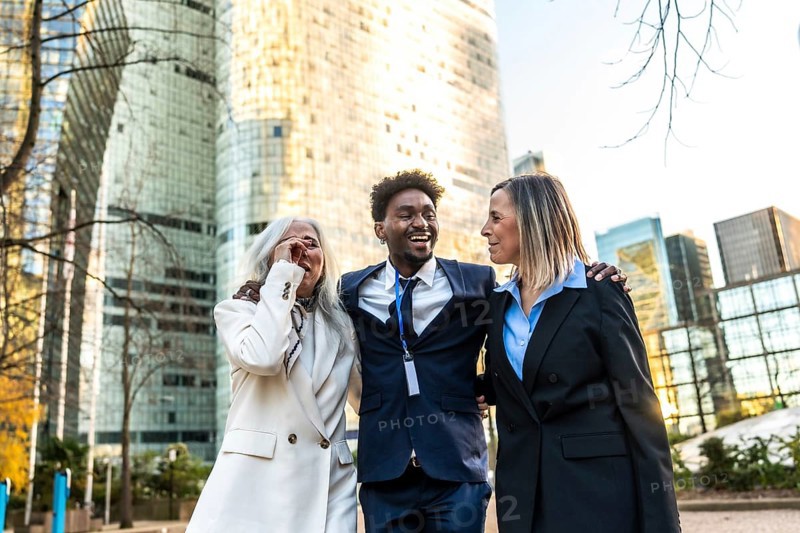Diverse business colleagues laughing and enjoying friendship while walking together on a metropolitan street with modern office buildings in the background