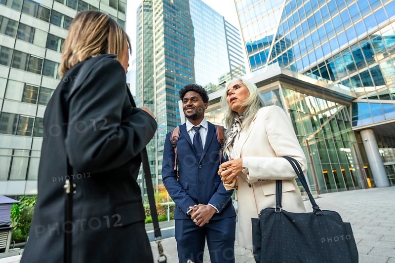 Diverse business professionals holding an informal outdoor meeting on a city street, exchanging ideas and collaborating against a backdrop of modern skyscrapers, teamwork and partnership
