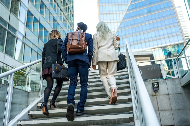 Diverse business colleagues moving upwards on an outdoor staircase in a contemporary city environment, representing aspiration, career advancement, and collective progress in the corporate world