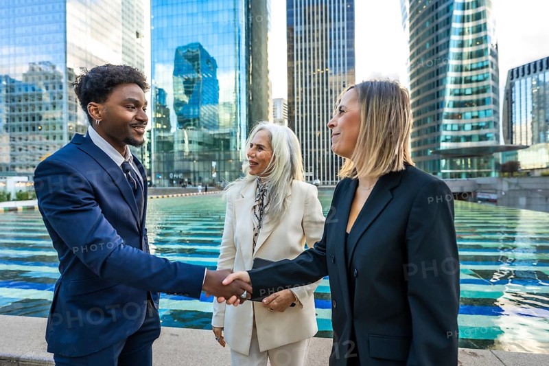 Diverse business people making a deal, shaking hands outdoors in a modern city corporate environment with skyscrapers, representing global partnership and successful negotiation