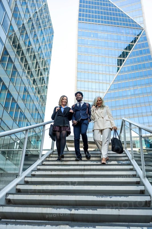 Diverse group of business people collaborating and walking down stairs in a modern financial district, reflecting concepts of teamwork, urban life, and professional progress