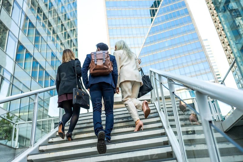 Business professionals ascending modern outdoor stairs in an urban financial district, moving with purpose towards career growth and professional achievement amidst tall glass buildings