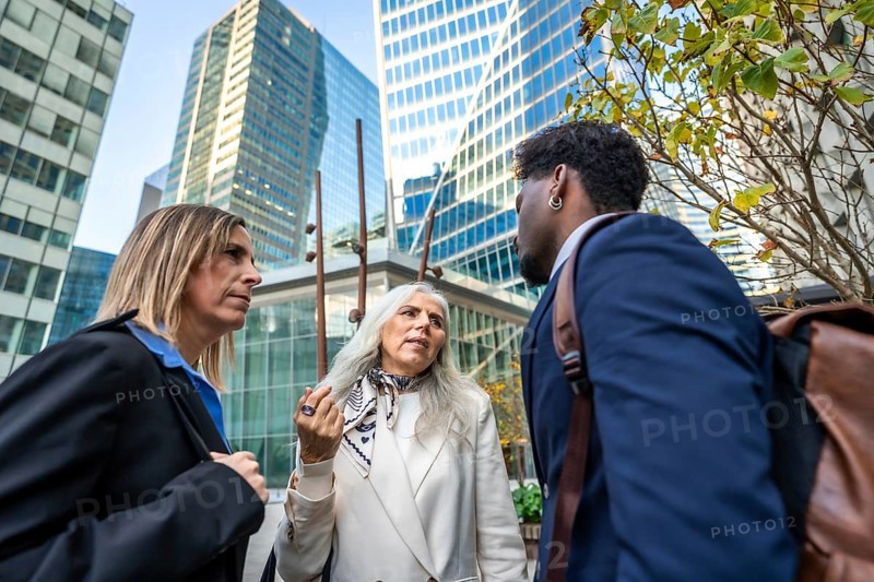 Professionals engaging in a focused conversation outside office buildings, representing collaboration, teamwork, and modern corporate communication in a city environment