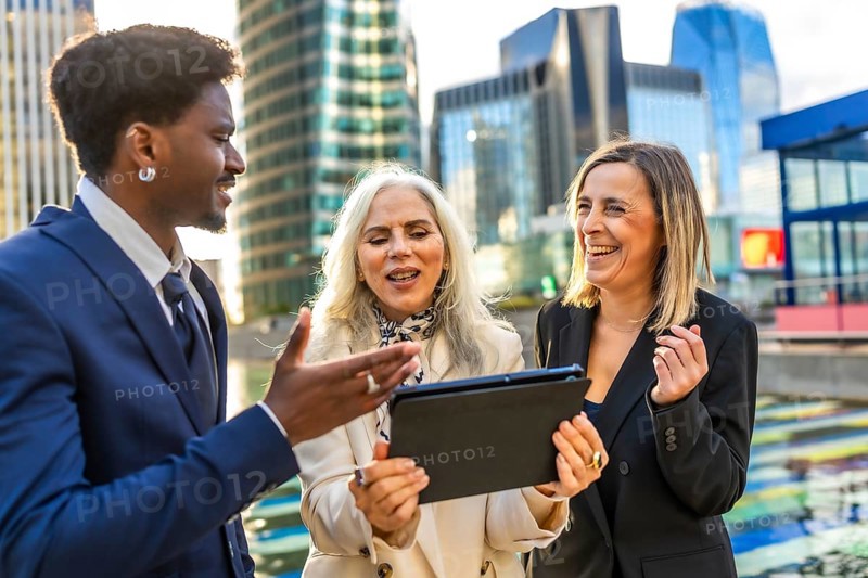 Diverse business professionals having an animated outdoor meeting, looking at a digital tablet and collaborating on a new project surrounded by a modern cityscape