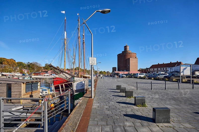 Round silo, historic brick building, architect Heinrich Hansen, architectural style New Objectivity, harbor basin, wharf, ships, general architecture, street, barrier bollard, lantern, parking boxes with cars, trees, blue sky, cloudless, Hafenstraße, Eckernförde, Rendsburg-Eckernförde district, Schleswig-Holstein, Germany
