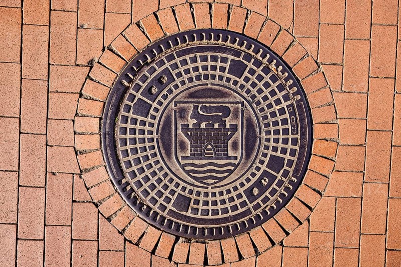 Manhole cover, city coat of arms, paving brick footpath, sunny, Eckernförde, Rendsburg-Eckernförde district, Schleswig-Holstein, Germany
