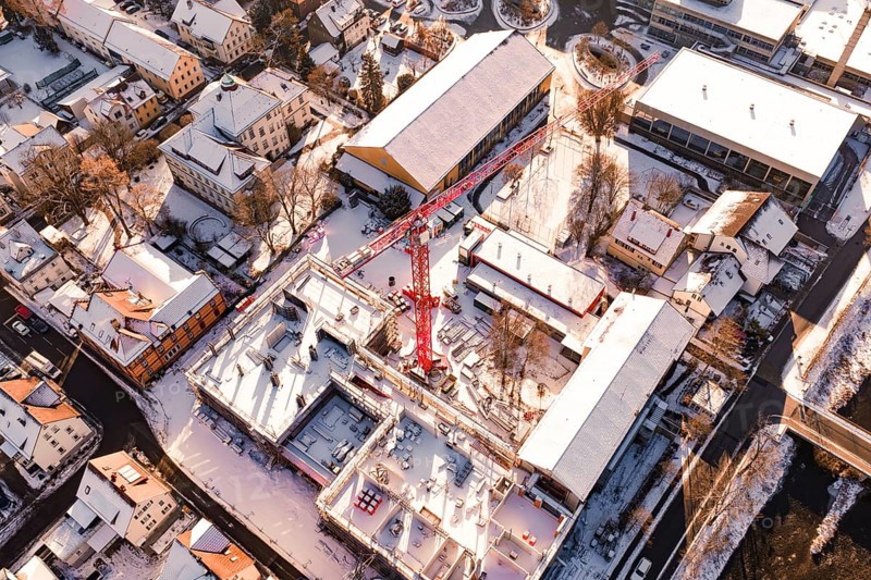 Bird's eye view of snow-covered city with construction crane and surrounding buildings in warm sunlight, Neubau Zellerschule, Nagold, Black Forest, Germany